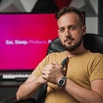 Man sitting in front of a pink screen with the text Eat Sleep Produce