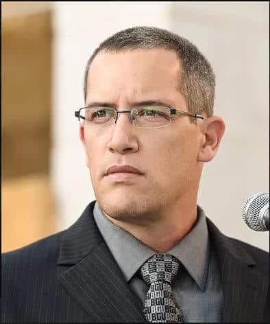 Man in glasses and suit with BGU tie next to a microphone