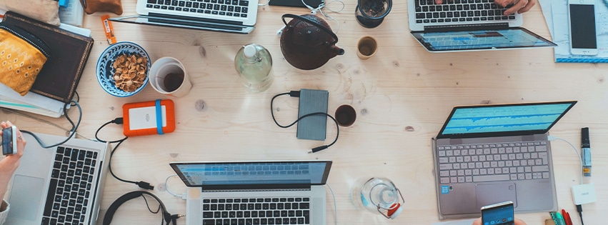 A shared desk with laptops, smartphones, and drinking cups